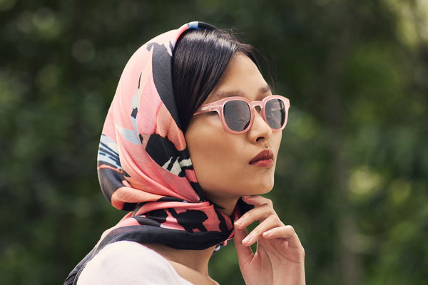 Photograph of a female model wearing the Olivia Newton-John Limited Edition Scarf covering her hair with the Trapeze Sunglasses in pink